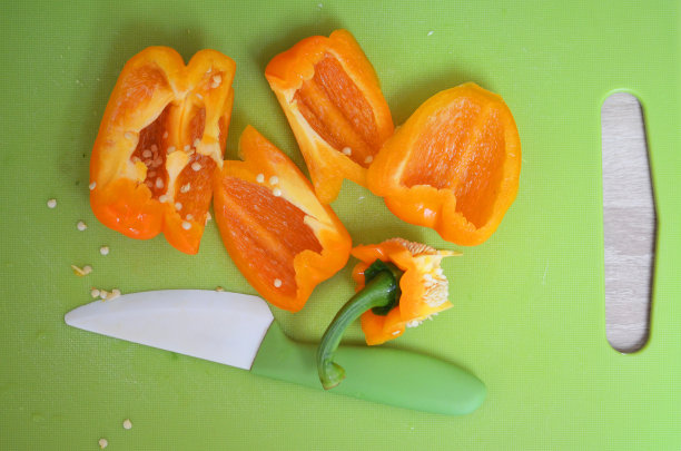 用绿色陶瓷刀将橙色甜椒切在绿色砧板上图片下载