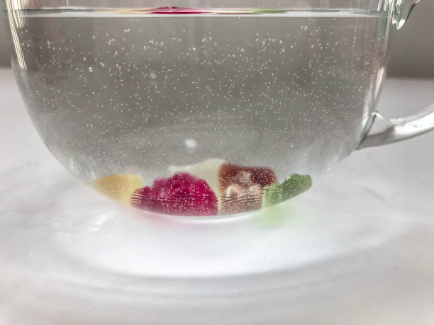 透明大杯，圆形，装满水。杯子底部是小熊软糖。熊的倒影在水中，大量和不均匀的糖果图片下载