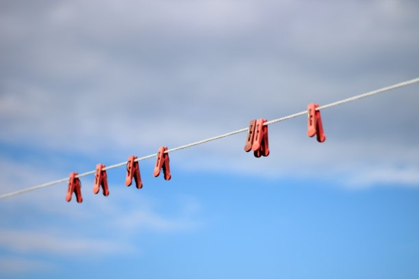 白色晾衣绳和红色塑料晾衣夹映衬着湛蓝的天空和云彩图片下载