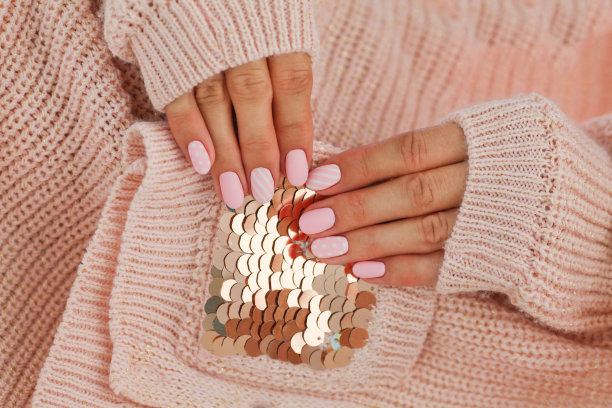 女性的手与美丽的椭圆形指甲，哑光粉色美甲近距离在粉红色针织毛衣的背景。图片下载