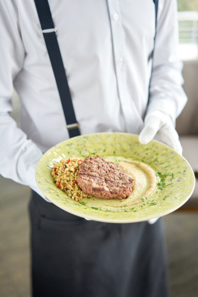 侍者端着一个盘子，上面放着有大理石花纹的牛排，还有烤干番茄干和烟熏洋葱奶油。烧烤餐厅的菜单，一系列不同肉类的照片图片下载