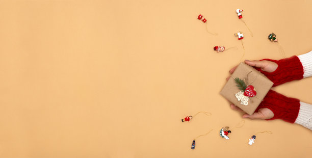 手在编织的手套拿着礼物和零浪费圣诞装饰在橙色的背景图片下载