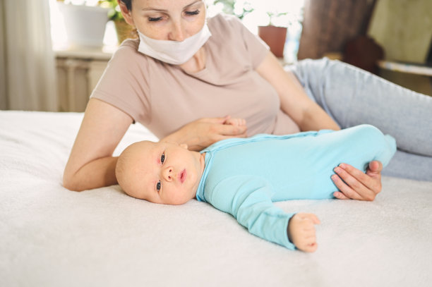 美丽的母亲戴着防护口罩，抱着她可爱的新生儿子，保护他免受病毒和感染。冠状病毒covid-19预防。居家隔离。幸福的家庭。图片下载