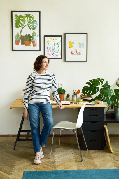 女艺术家在家工作站在她的工作单位旁边，微笑。自由插画家在她的工作室创造新的项目图片下载