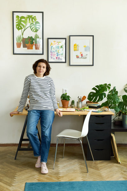女艺术家在家工作站在她的工作单位旁边，微笑。自由插画家在她的工作室创造新的项目图片下载