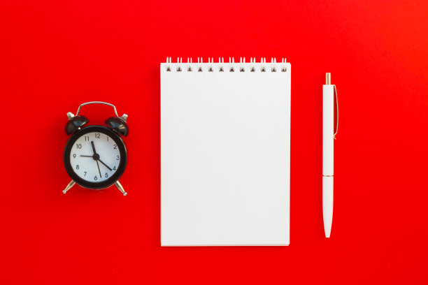 空白记事本，钢笔和迷你闹钟在红色的背景。时间管理。笔记本的想法，信息，清单和灵感。模型为您的设计。俯视图，平躺与复制空间。图片下载