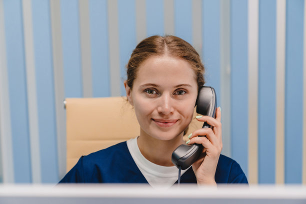 年轻的白人女接待员在诊所里打电话，同时坐在那里看着摄像机图片下载