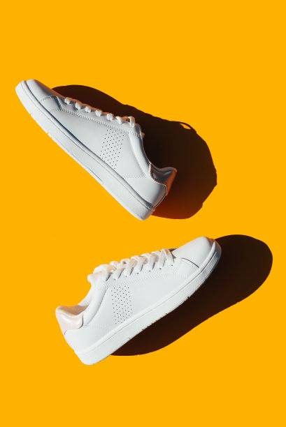 白色运动鞋在橙色的背景和硬阴影。图片下载
