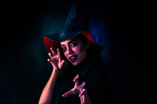 万圣节派对女孩。万圣节女巫明亮的妆容和长发。美丽的年轻惊讶的女人摆着女巫性感的服装。复古风格的背景图片下载