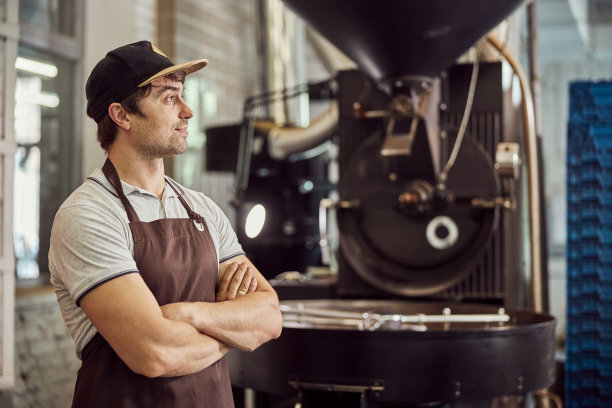英俊的男工人站在咖啡烘焙机旁图片下载
