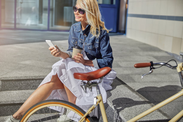 穿着牛仔夹克的快乐微笑的女人坐在城市街道的台阶上图片下载