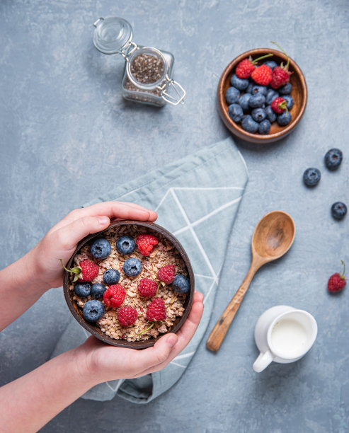 手孩子保持椰子碗与麦片和浆果在蓝色的背景图片下载