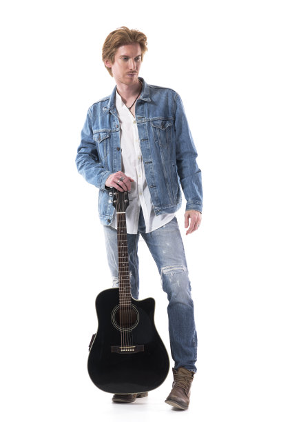 严肃沉思的年轻男子吉他手在牛仔裤看着下拿着吉他乐器。图片下载