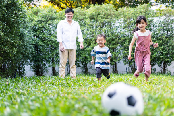 亚洲大家庭一起在花园操场上玩耍。孩子们跑着和爸爸一起在绿色的草地上踢足球，感觉很有趣。快乐的家庭和兄弟姐妹享受爱的活动理念。图片下载