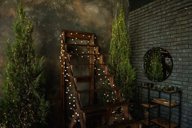 一段棕色的木楼梯上挂着许多明亮的灯，靠着一堵破旧的灰色混凝土墙。阁楼上的圣诞树。砖面有一面圆镜子，下面有一个黑色的架子。图片下载