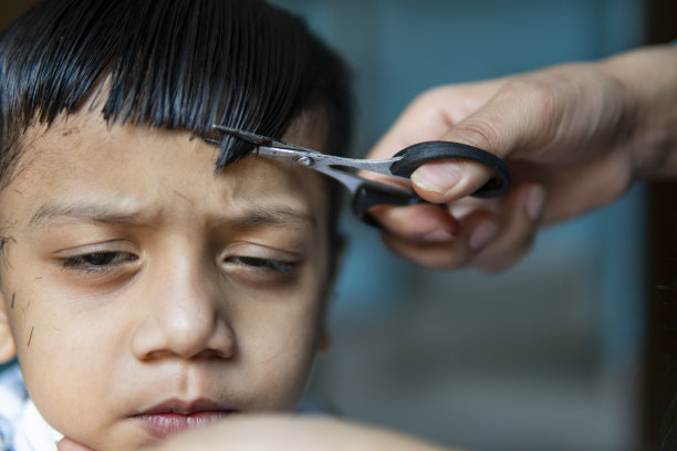 母亲的手在家里剪她孩子的头发的特写。图片下载