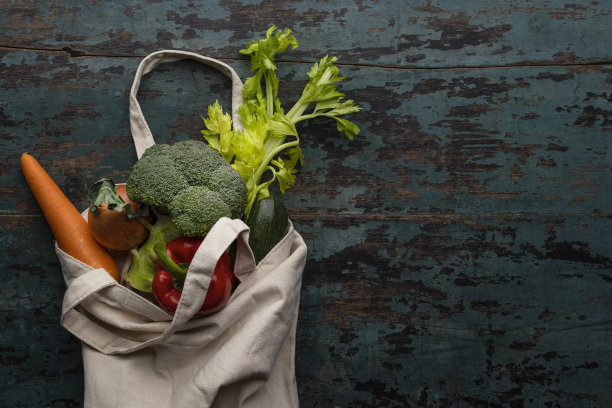 许多色彩对比丰富的市场新鲜蔬菜在一个可重复使用的天然棉花购物袋在一个古老的风化木绿松石颜色的桌子背景。图片下载