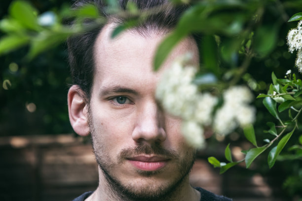 这是一幅创造性的白人男性肖像，一只眼睛被春天的花朵遮住了图片下载
