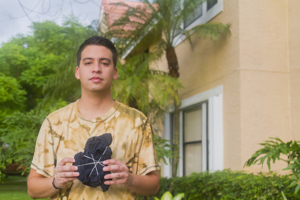 在新冠病毒期间，手持扎染T恤的拉丁裔年轻男子肖像图片下载