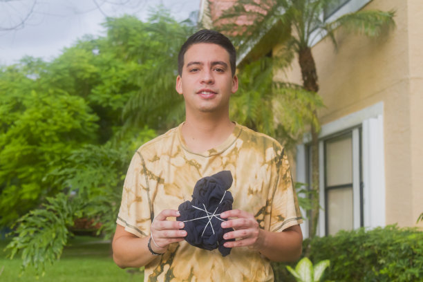 在新冠病毒期间，手持扎染T恤的拉丁裔年轻男子肖像图片下载