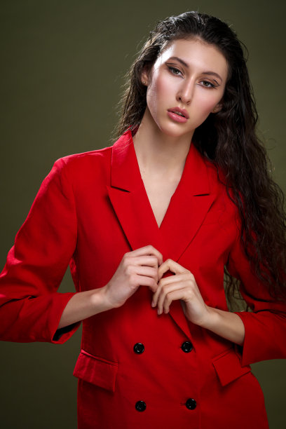 一个性感的年轻女子的肖像，穿着红色夹克，与潮湿的黑色长头发在工作室的绿色背景下摆姿势。图片下载