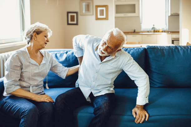 老夫妇在家。英俊的老男人背痛，他的迷人的老女人支持他。图片下载