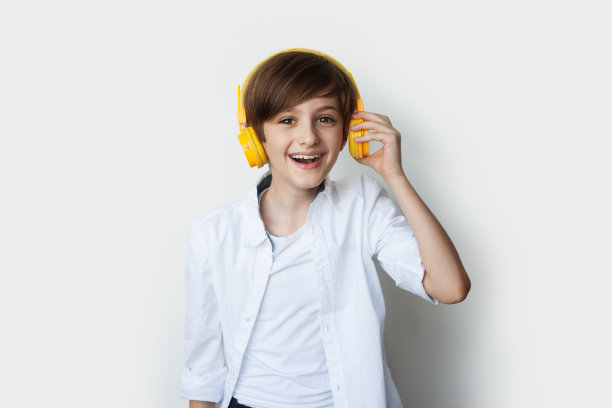 年轻的白人男孩通过耳机在一个白色的录音室背景下听音乐图片下载