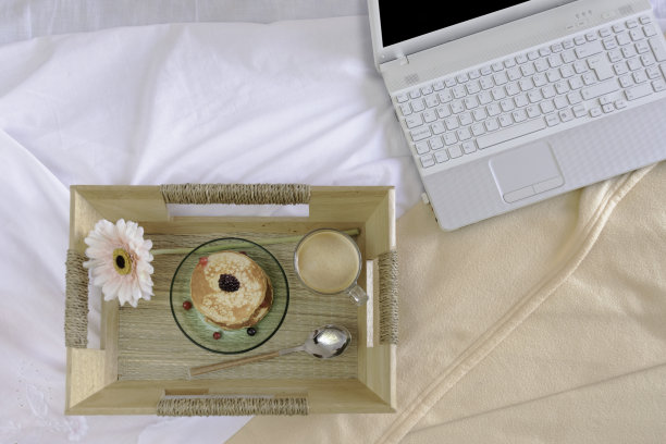 早餐在床上。白色的床，托盘上放着咖啡和煎饼。图片下载