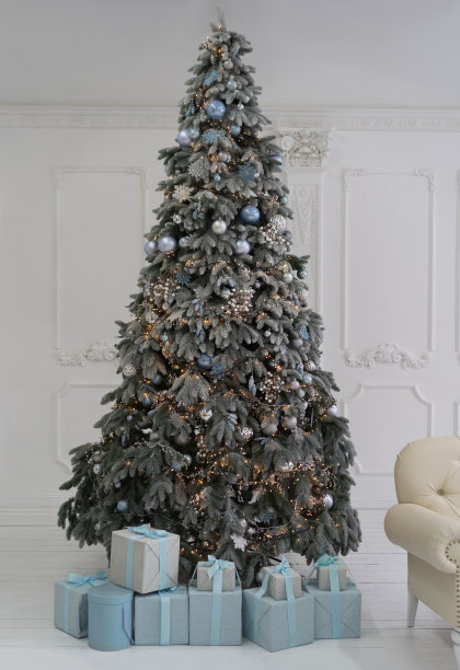 一棵巨大的圣诞树，靠在白色的墙上。圣诞树下放着盒子里的礼物，用丝带装饰着。在圣诞树上的球和花环上。高质量的照片图片下载