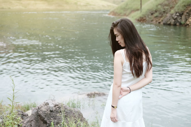 亚洲妇女穿着白色的衣服是微笑附近的河流在森林。自由生活在自然的概念。图片下载