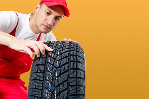 汽车技工携带轮胎在黄色的背景。快乐的人看着镜头微笑图片下载