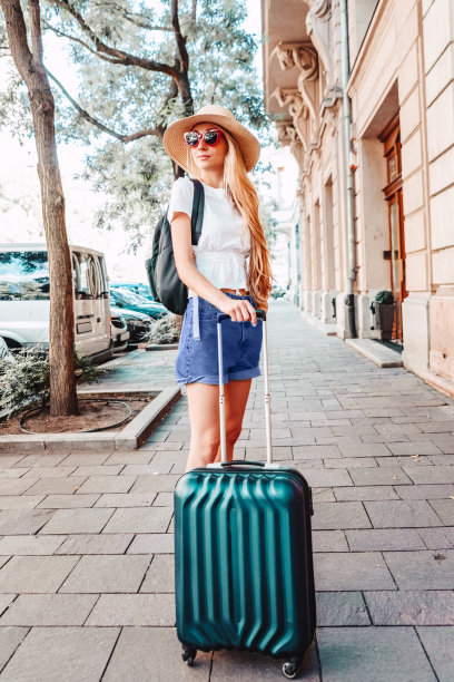 这是一名年轻女子在城市度假时提着行李箱走在街上的照片图片下载