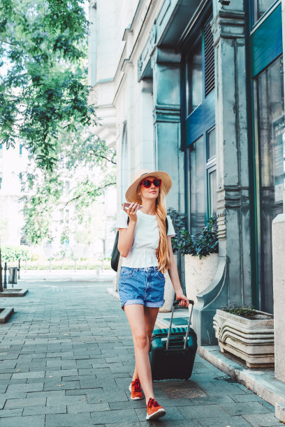 这是一名年轻女子在城市度假时提着行李箱走在街上的照片图片下载