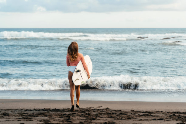 年轻迷人的冲浪女子与白板在日落的海洋上。印度尼西亚巴厘岛。图片下载