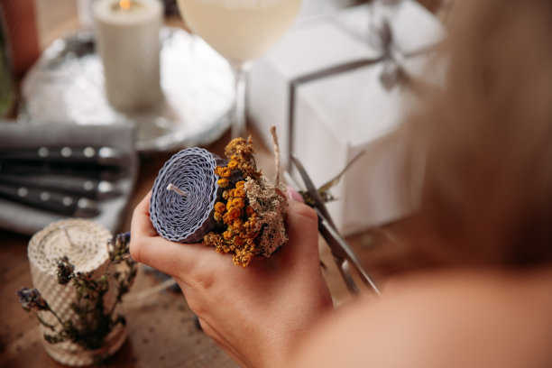 DIY蜡烛制作过程。女人做装饰蜡蜡烛和装饰干花，手的特写图片下载