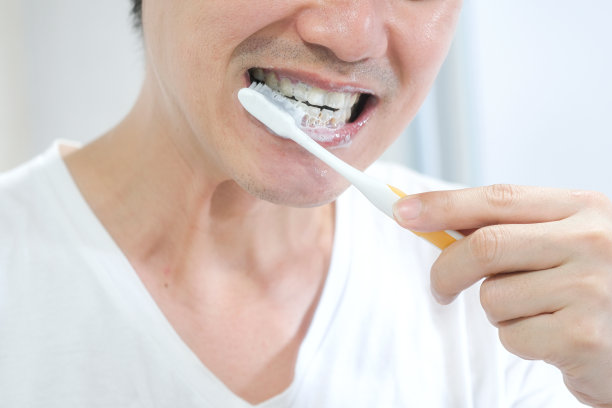 一个年轻的亚洲人，他用牙刷和牙膏清洁牙齿。图片下载