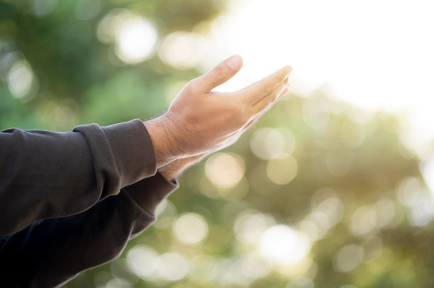 在自然的背景下，在阳光的照射下，祈祷的男性的双手伸向天空，祈求希望。宗教和信仰观念。图片下载