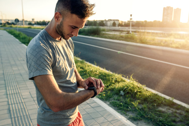 年轻帅气的运动慢跑者从户外运动中休息，看一个智能的健身手表图片下载
