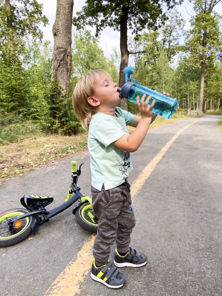 在森林里，皮肤白皙的小孩用运动瓶喝水。图片下载