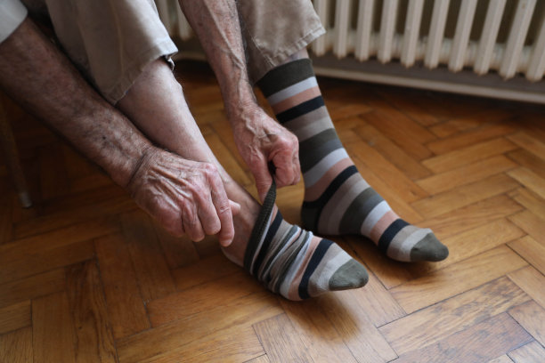 一个高级男子的特写穿着坐在椅子的边缘上穿或脱下一双彩色的袜子图片下载