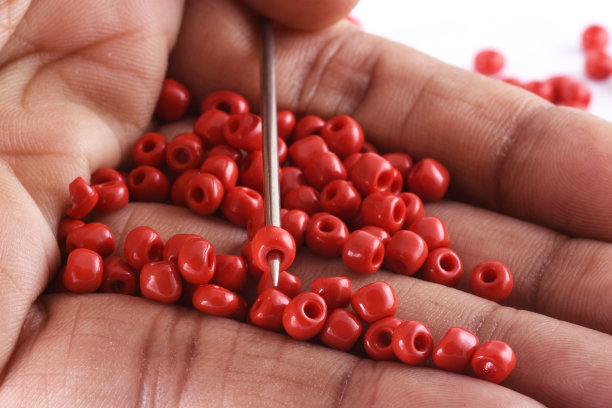 一个女人的手钉珠子在针上的特写照片。珠针。宏，用于整理时装服装。制作串珠项链，时尚女性串珠，串珠钩针。每天的珠饰。图片下载