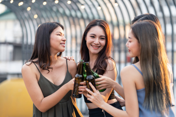 年轻可爱的亚洲女孩在屋顶餐厅聚会，喝啤酒庆祝的欢乐场景图片下载