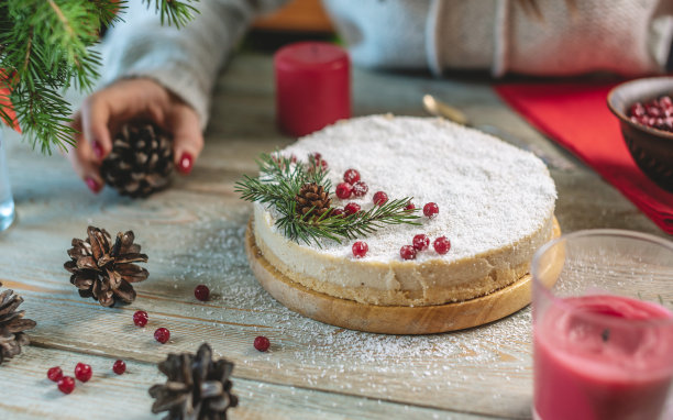 节日的白色慕斯蛋糕，上面覆盖着仿雪的椰子片，用红浆果、松果和杉树枝装饰。新年和圣诞节的概念图片下载