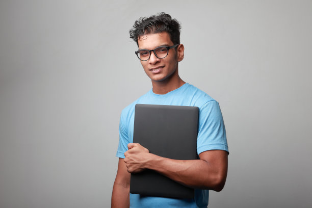 一个印度裔年轻人手里拿着一台笔记本电脑图片下载