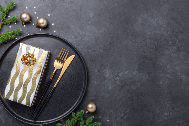 圣诞餐桌设置黑色陶瓷盘子，礼盒和黄金配件在黑色的石头背景。为你的文本复制空间图片下载