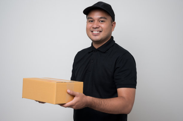 工人亚洲快递员在黑色制服拿着盒子包裹纸板给客户站在孤立的白色背景。图片下载