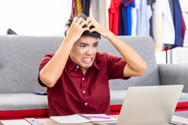 年轻的亚洲男性在线商人自由博主正在用笔记本电脑在家办公，遇到了严重的问题。社交媒体，不成功的，网上购物的概念。图片下载