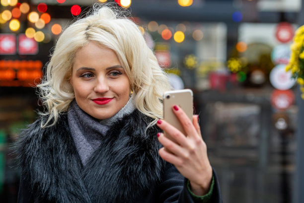 年轻，美丽的金发女人在节日的灯光背景下自拍。圣诞节的时间概念。副本的空间。图片下载