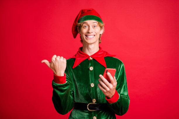 照片的积极精灵家伙拿着智能手机点拇指手指空空间圣诞折扣广告孤立在红色背景。图片下载