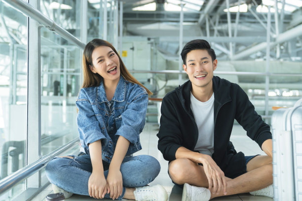 年轻的亚洲休闲装度假旅行夫妇朋友坐放松大笑一起微笑在地板在公共空间安全旅行新常态的生活方式等待时间时刻表，登机离开图片下载